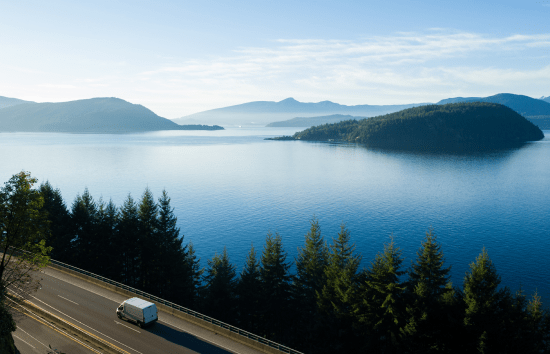 White van traveling along road near a lake