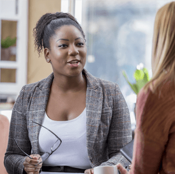 Mujer sentada y hablando con otra mujer en el trabajo.